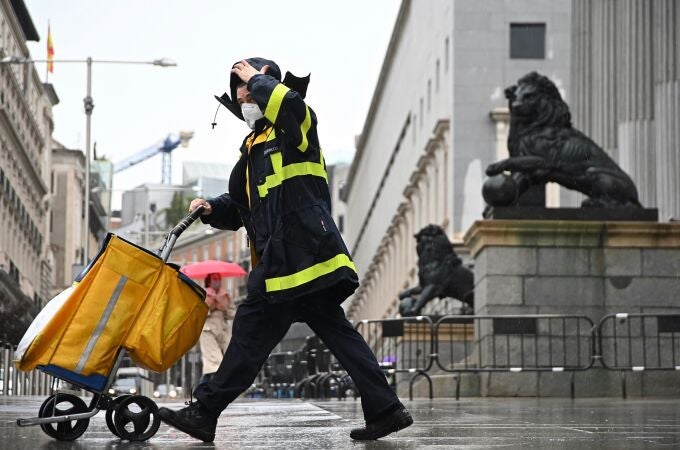 Un trabajador de Correos, bajo la lluvia, a su paso por el Congreso de los Diputados de Madrid