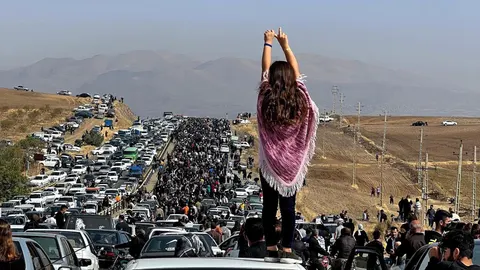 Una mujer sin velo encima de un vehículo mientras miles de personas se dirigen al cementerio de Aichi en Saqez, la ciudad natal de Mahsa Amini en la provincia occidental iraní del Kurdistán, para conmemorar los 40 días de su muerte