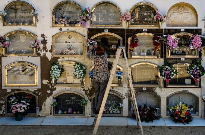 Una mujer coloca un ramo de flores en la lápida de un ser querido en un cementerio en Barcelona el Día de todos los Santos