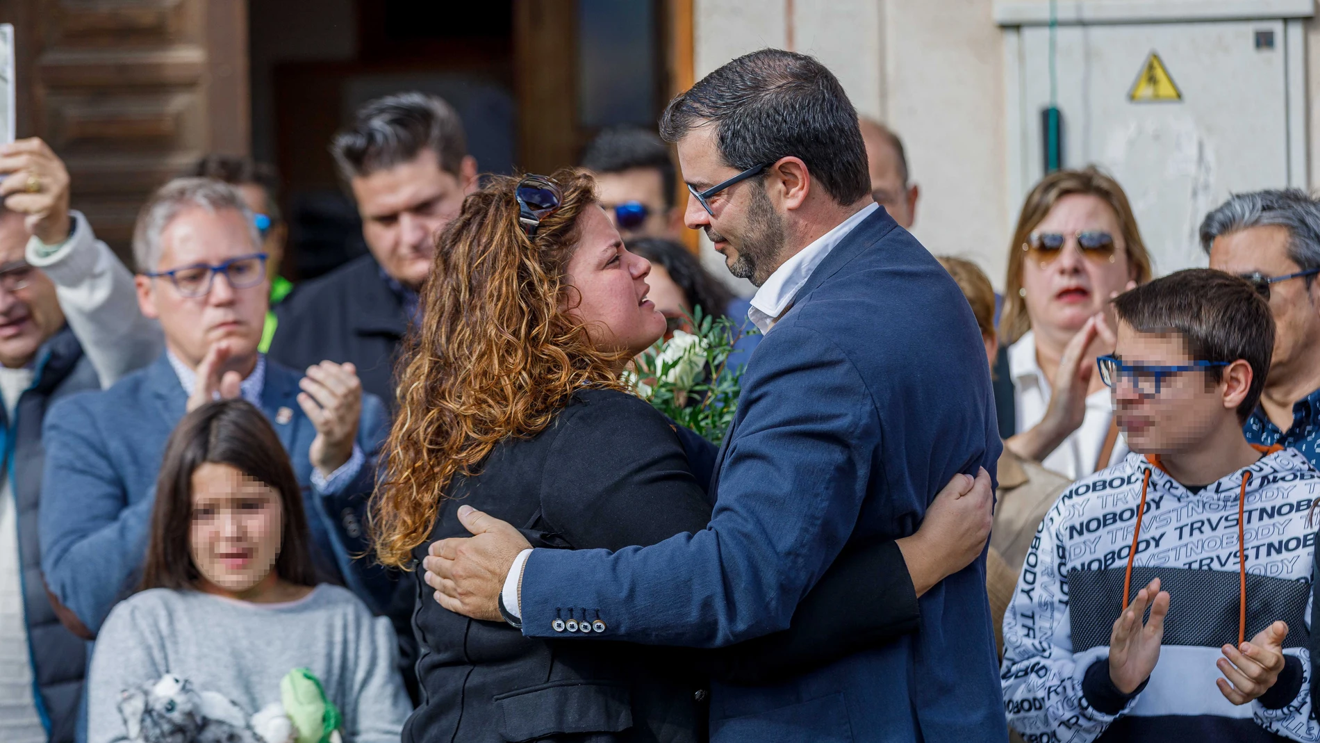 La tía de la niña asesinada junto al padre de la niña asesinada se abrazan durante un homenaje y minuto de silencio por la niña, en la Plaza Mayor de Torrecaballeros (Segovia)