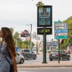 Una joven en manga corta pasa junto a un termómetro que marca 28 grados centígrados en Murcia