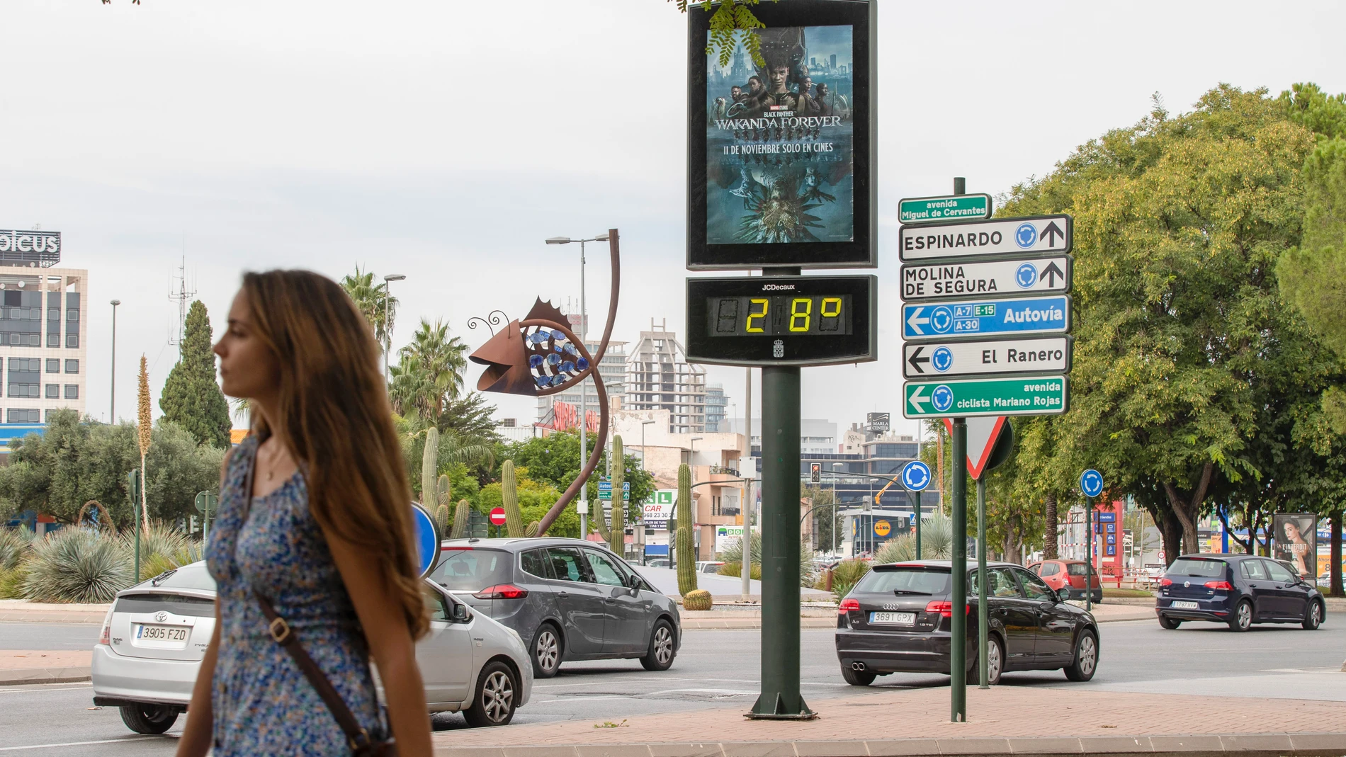 Una joven en manga corta pasa junto a un termómetro que marca 28 grados centígrados en Murcia