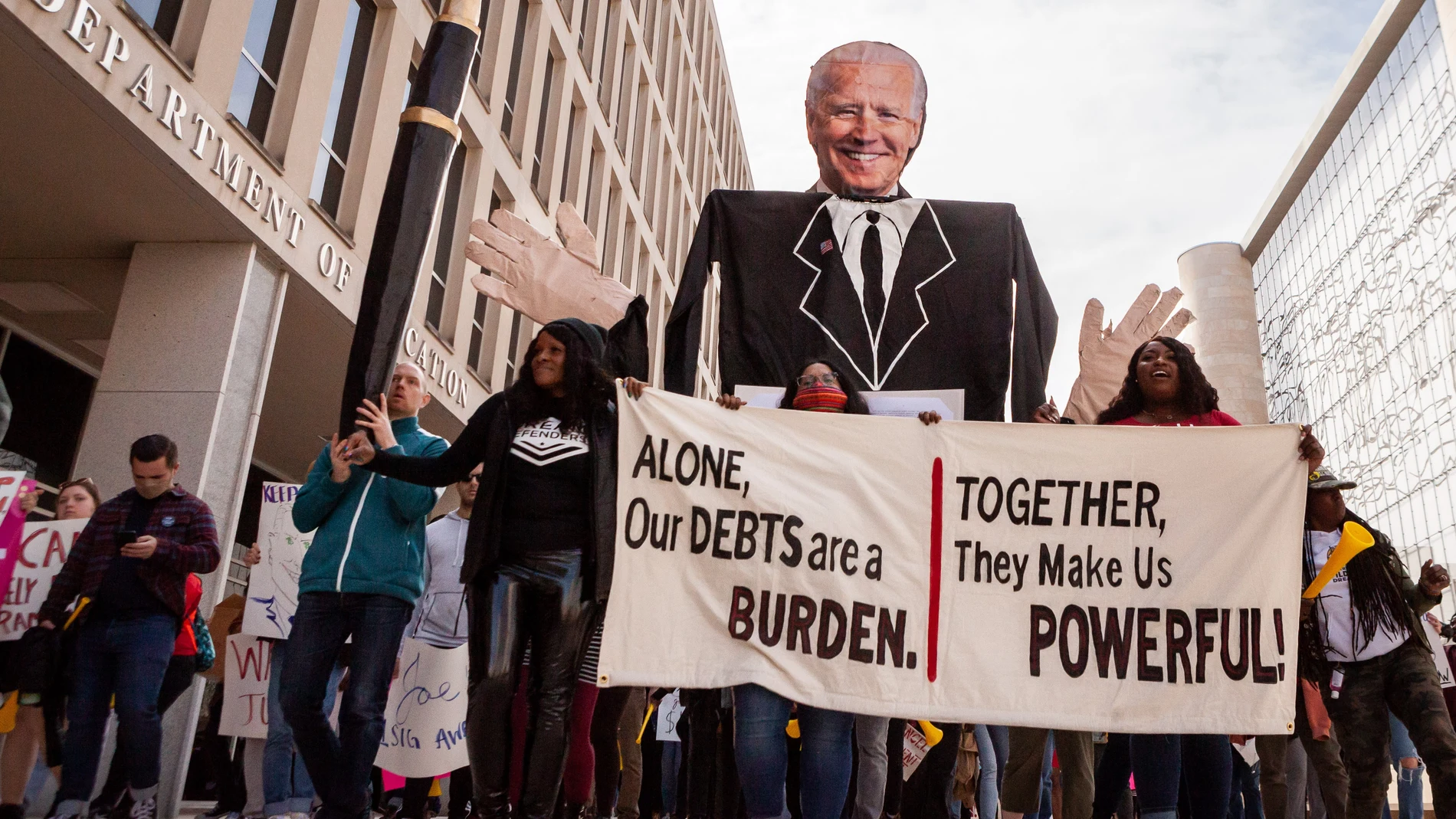 Manifestantes marchan con una pancarta y un cartel de Biden alrededor del Departamento de Educación durante una manifestación para pedir la condonación de deudad universitarias11/11/2022