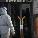 Un trabajador con traje protector camina frente a los avisos de cierre colocados en un café como parte de los controles de COVID-19 en Beijing.