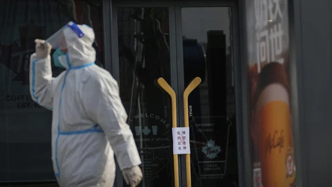 Un trabajador con traje protector camina frente a los avisos de cierre colocados en un café como parte de los controles de COVID-19 en Beijing.