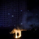 KUn hombre cerca de basura ardiendo frente a un edificio de apartamentos durante un corte de electricidad programado en Kyiv. Detrás, un edificio de apartamentos sin luz