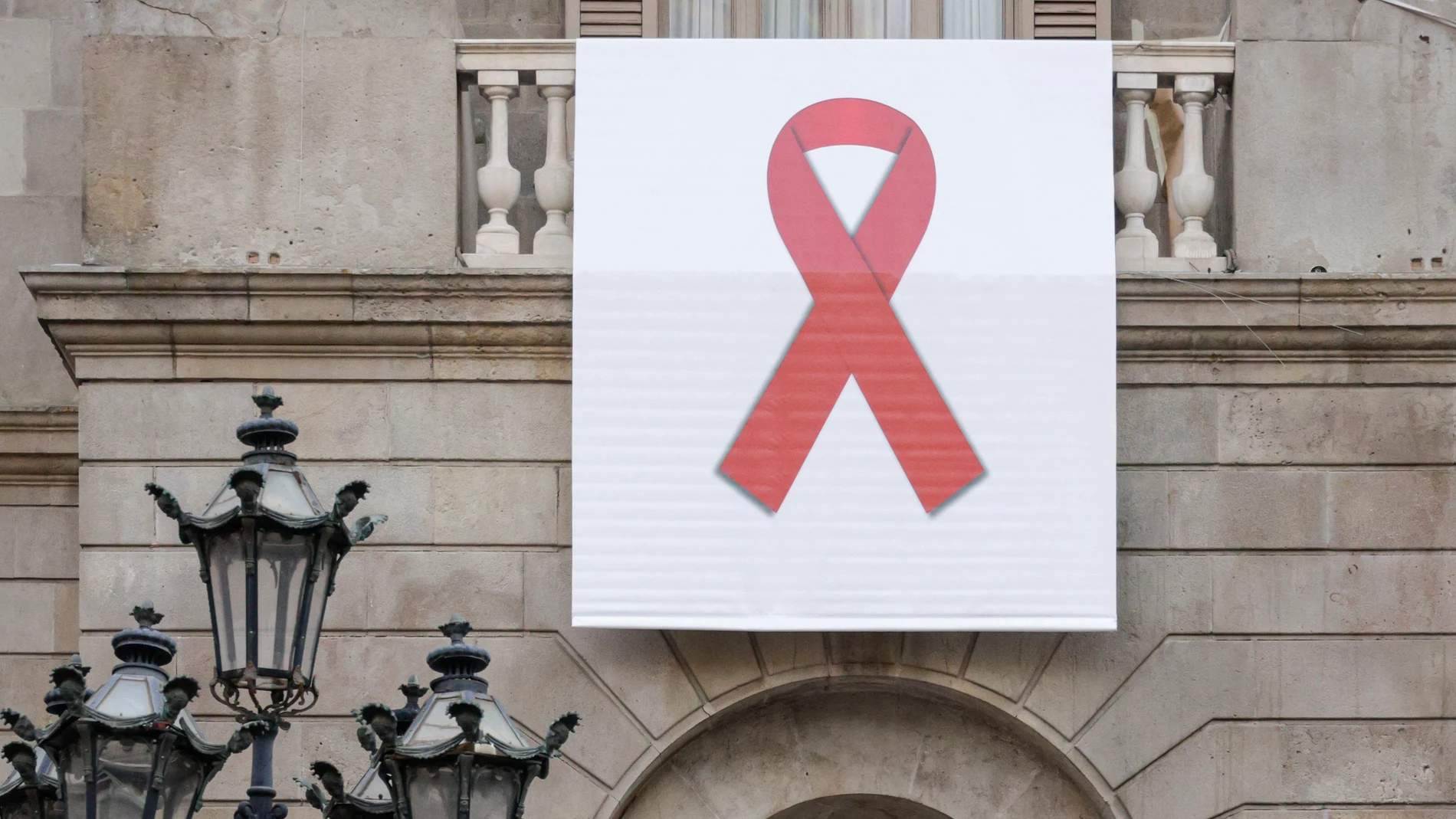 El ayuntamiento de Barcelona colgó en su balcón un lazo rojo gigante para sensibilizar, visibilizar y mostrar su apoyo a las personas que viven con el VIH durante la conmemoración hoy del Día Mundial de la lucha contra el sida