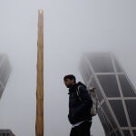 Un hombre pasa por delante de la Puerta de Europa o popularmente conocidas como 'Torres KIO' cubiertas de niebla