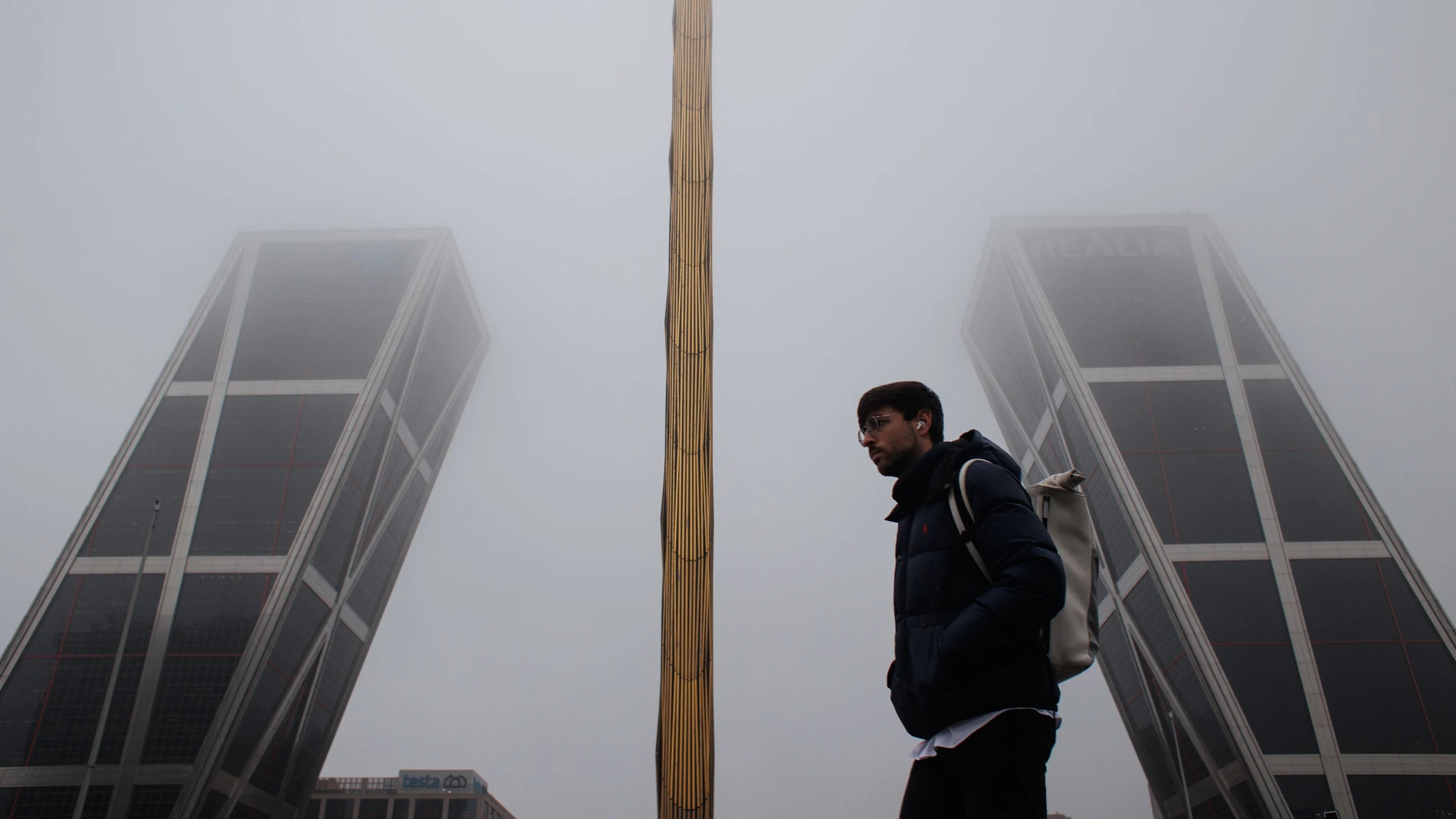 Un hombre pasa por delante de la Puerta de Europa o popularmente conocidas como 'Torres KIO' cubiertas de niebla