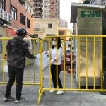 Una mujer con mascarilla atraviesa una barricada alrededor de una comunidad cerrada para recibir un paquete en Shanghai