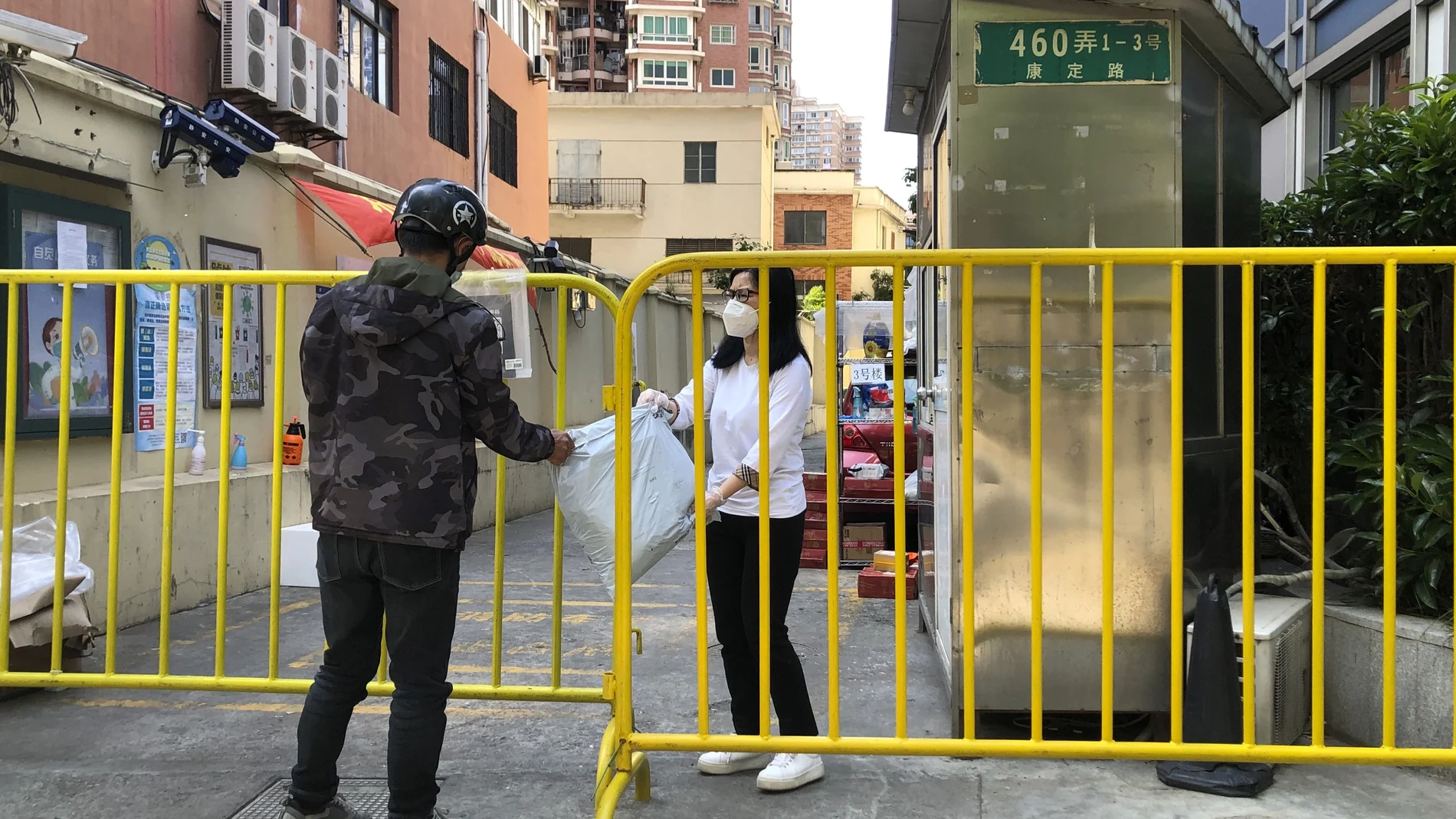 Una mujer con mascarilla atraviesa una barricada alrededor de una comunidad cerrada para recibir un paquete en Shanghai