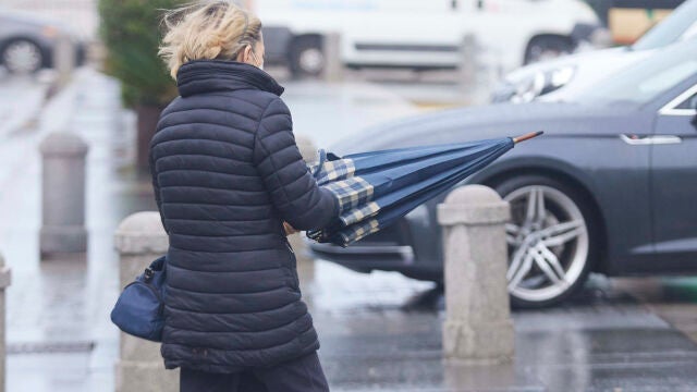 Una señora cierra el paraguas por el fuerte viento
