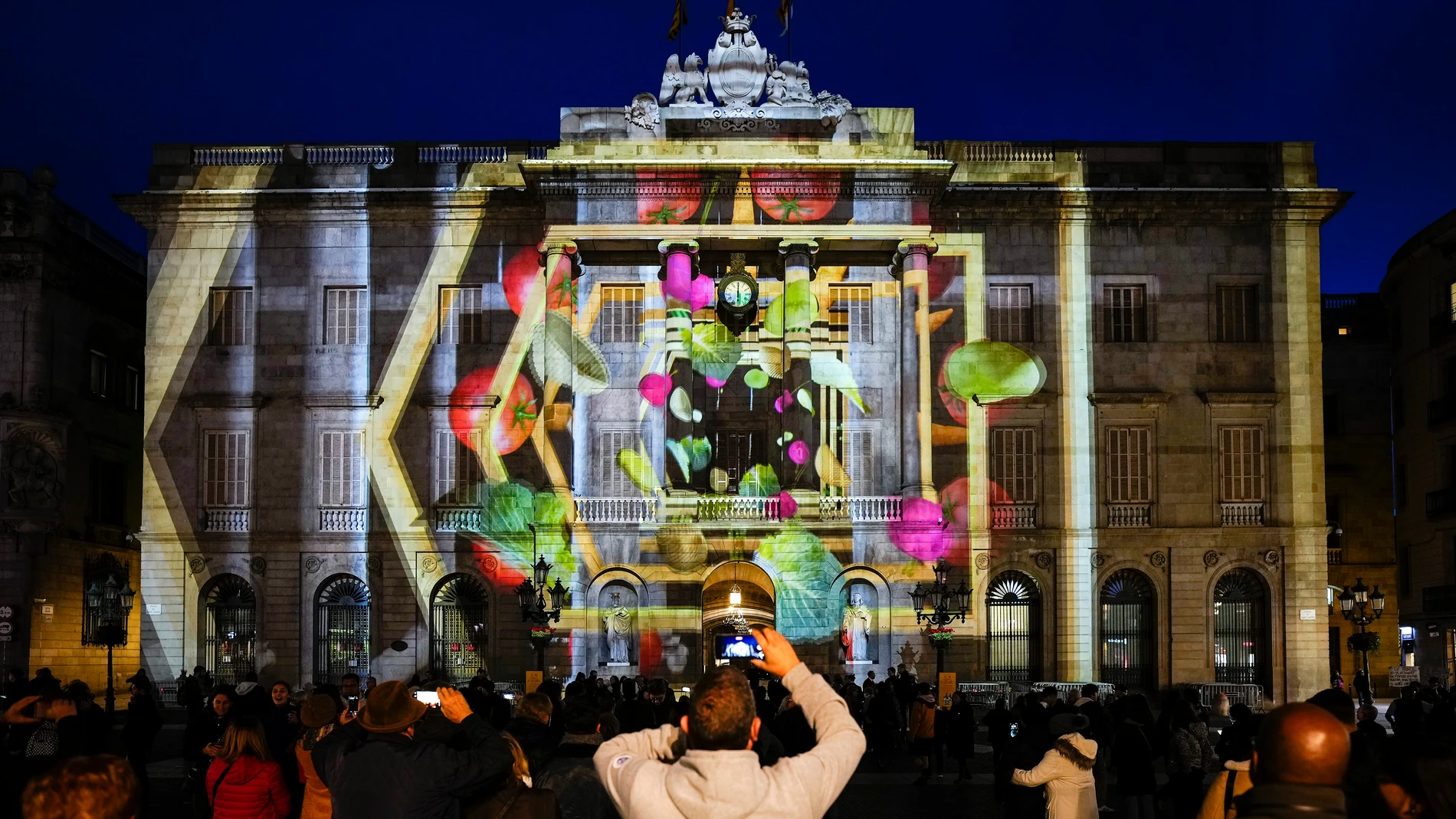 Varias personas disfrutan este viernes del inicio de las proyecciones del pesebre digital en formato de video 'mapping' en la fachada del Ayuntamiento de Barcelona