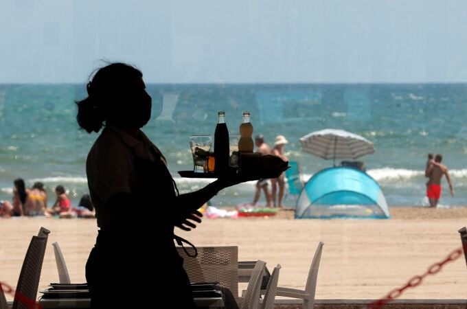 Una camarera lleva una bandeja en la playa valenciana de la Malvarrosa