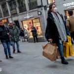 Una mujer camina con varias bolsas de compras y con mascarilla