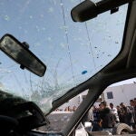 El parabrisas dañado de un coche mientras los palestinos (detrás) inspeccionan los vehículos dañados tras una incursión de las fuerzas israelíes en Yenin, Cisjordania