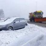 Un coche cubierto de nieve y una máquina quitanieves en la carretera de acceso al Puerto de Navacerrada