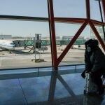 Un hombre con mascarilla se sienta sobre su maleta en el aeropuerto internacional de Pekín, China, este sábado