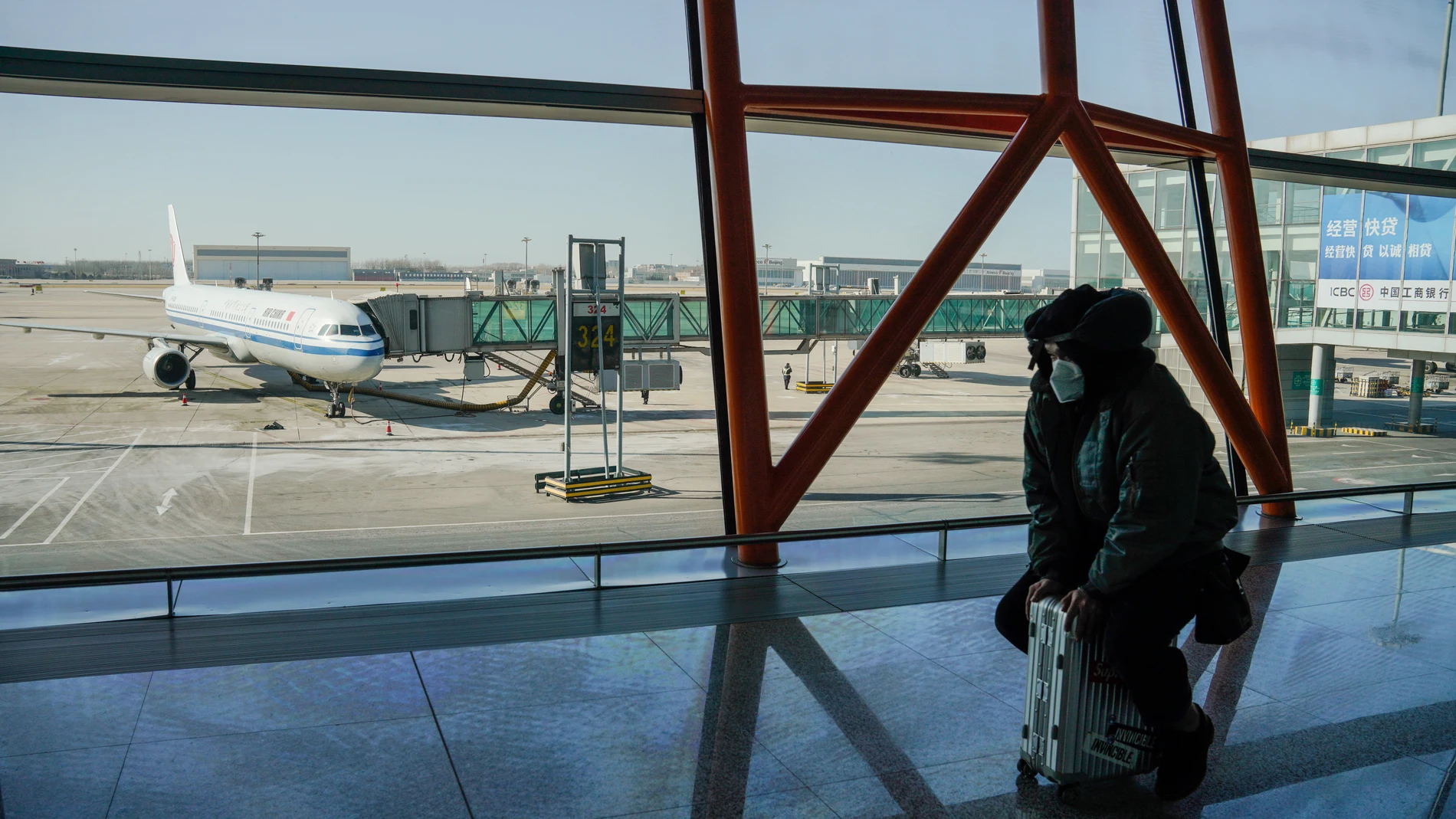 Un hombre con mascarilla se sienta sobre su maleta en el aeropuerto internacional de Pekín, China, este sábado