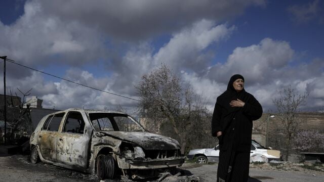 Una mujer palestina junto a un coche quemado en el pueblo de Jalud, cerca de la ciudad cisjordana de Naplusa