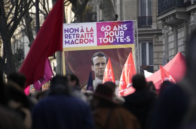 Manifestantes sostienen un cartel que muestra al presidente francés Emmanuel Macron y en el que se lee "No al plan de jubilación de Macron, 60 años para todos"
