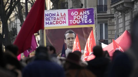 Manifestantes sostienen un cartel que muestra al presidente francés Emmanuel Macron y en el que se lee "No al plan de jubilación de Macron, 60 años para todos"