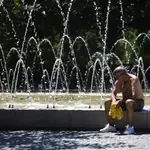 Un hombre descansa al lado de una fuente durante una de las olas de calor en Madrid 
