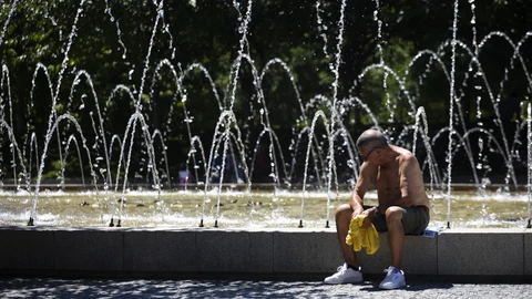 Un hombre descansa al lado de una fuente durante una de las olas de calor en Madrid
