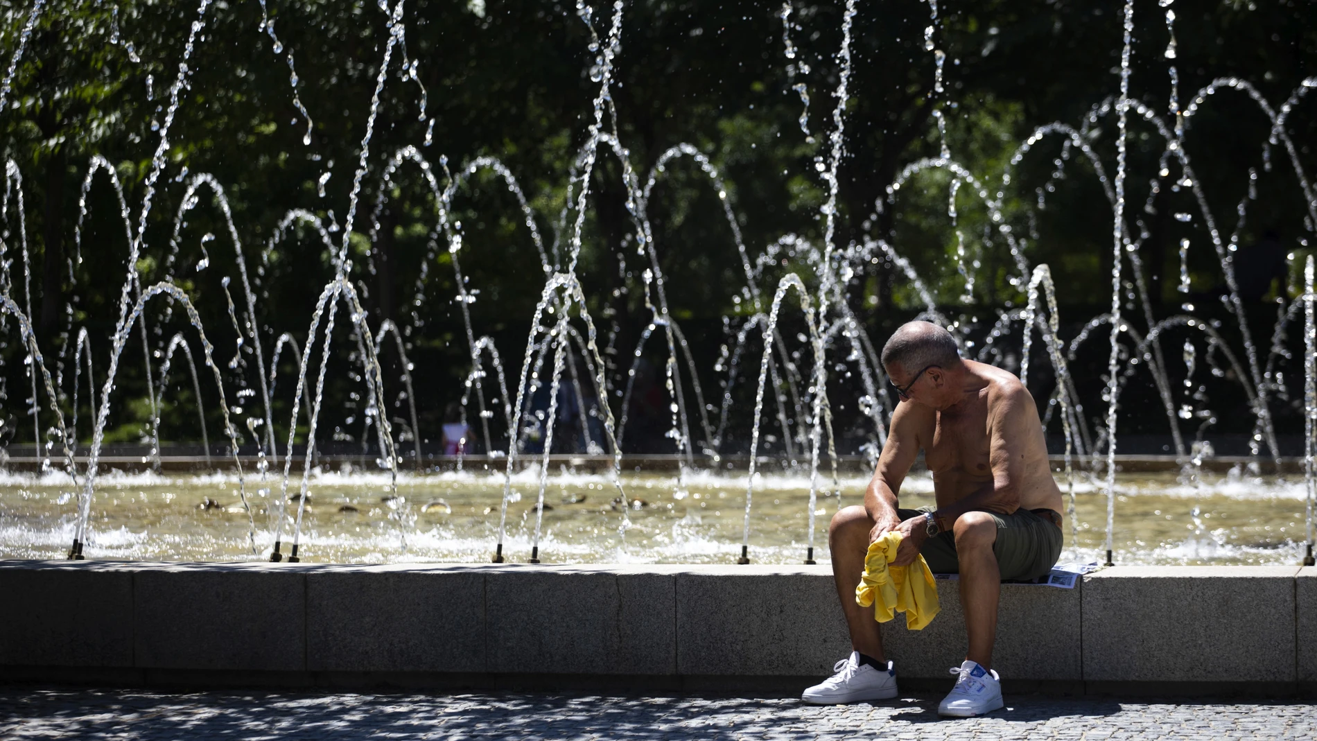 Un hombre descansa al lado de una fuente durante una de las olas de calor en Madrid