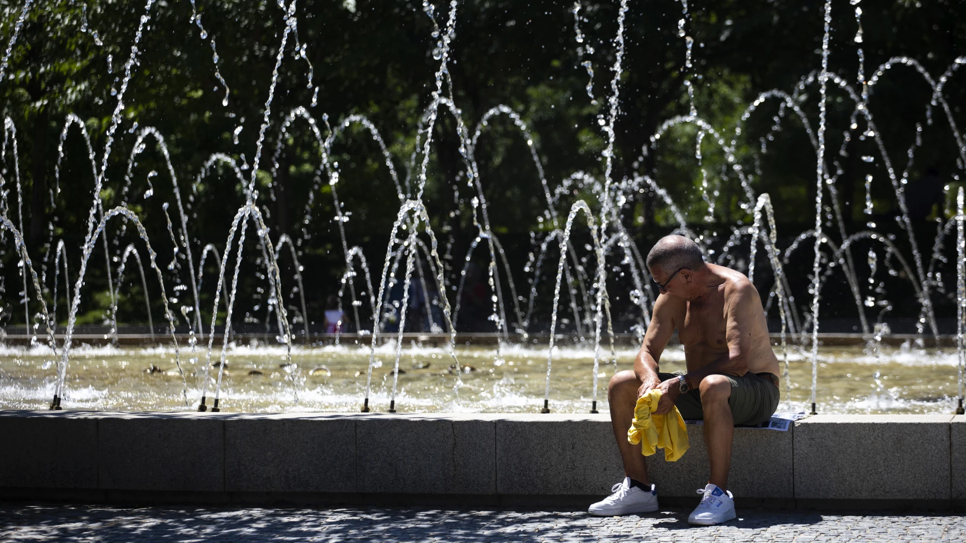Un hombre descansa al lado de una fuente durante una de las olas de calor en Madrid este verano