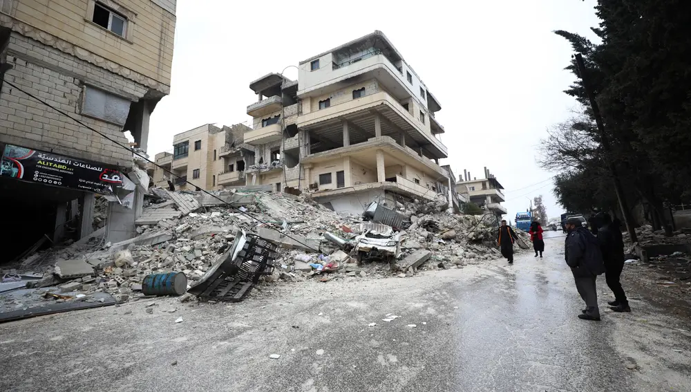 Varias personas caminan cerca de un edificio derrumbado tras un terremoto en la ciudad de Armanaz, en la gobernación siria de Idlib