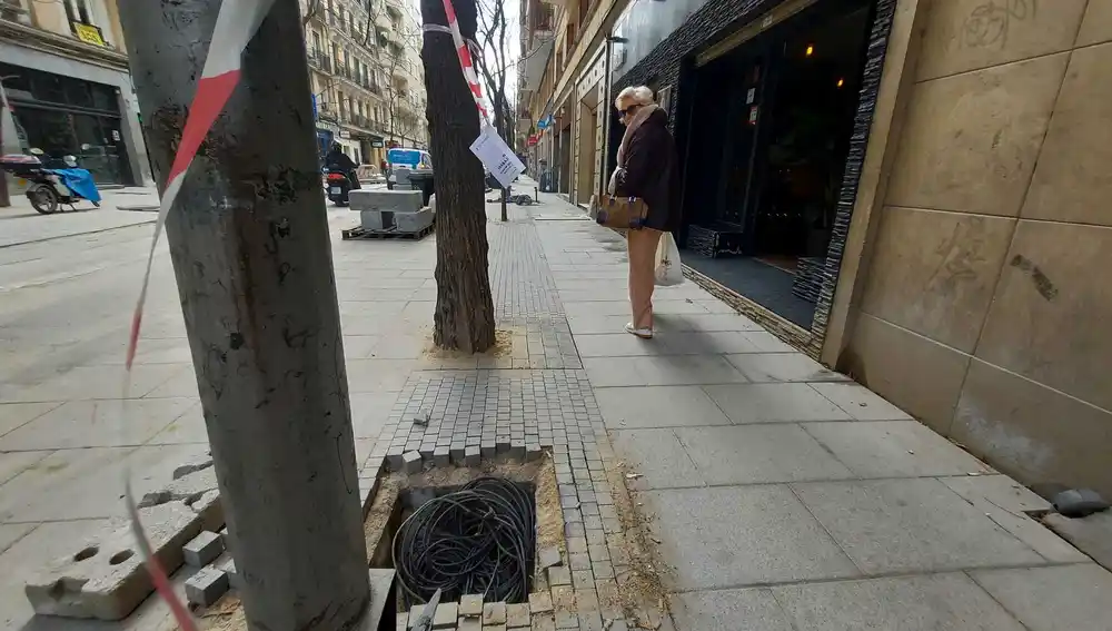Una señora paseo por la calle Ponzano y se gira a mirar un hoyo lleno de cables en la acera