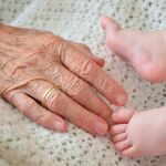 Mano una persona anciana junto a los pies de un infante. 
