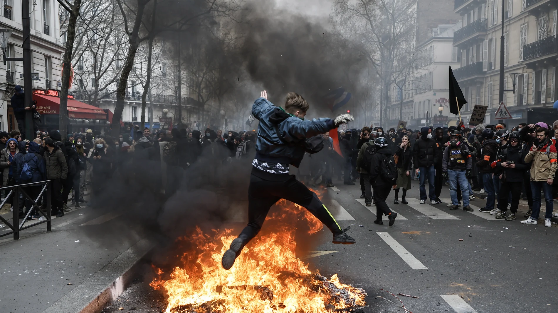 Un manifestante salta sobre un fuego durante la última jornada de protestas y huelgas contra la reforma de las pensiones de Emmanuel Macron, en París