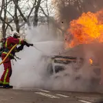 En París, un bombero apagando un incendio provocado por manifestantes a un coche, durante la manifestación contra la reforma de las pensiones