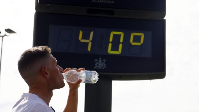Un joven bebe agua junto a un termómetro de calle que marca 40 grados