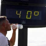 Un joven bebe agua junto a un termómetro de calle que marca 40 grados en el centro de Córdoba