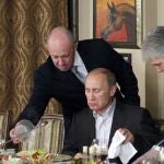 Businessman Yevgeny Prigozhin, left, serves food to Russian Prime Minister Vladimir Putin, center, during dinner at Prigozhin's restaurant outside Moscow, Russia, Friday, Nov. 11, 2011. 
