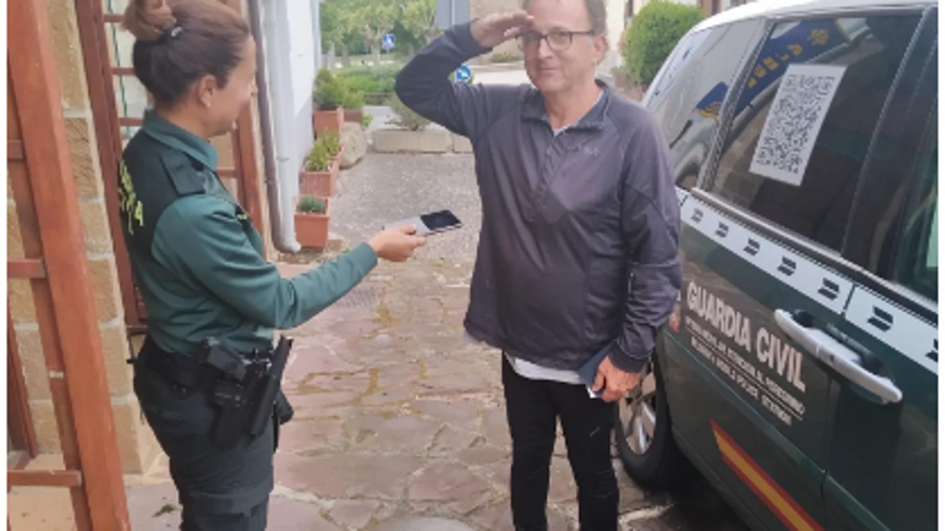 Un peregrino saluda militarmente a una agente que le hace entrega del móvil que había perdido