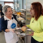 María Paz, voluntaria de 79 años, da la bandeja para la comida a Silvia, canaria de 59 años, en el comedor social Santiago Masarnau que cumple 25 años