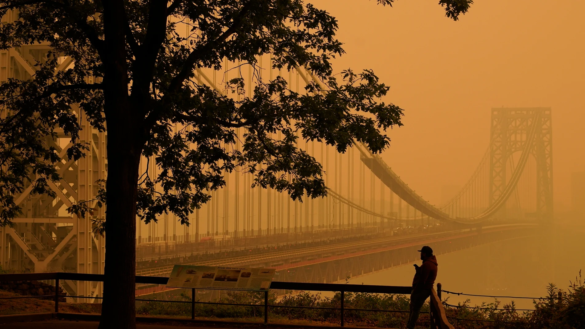 FILE - A man talks on his phone as he looks through the haze at the George Washington Bridge in Fort Lee, N.J., June 7, 2023. As smoky as the summer has been so far, scientists say it will likely be worse in future years because of climate change. (AP Photo/Seth Wenig, File)