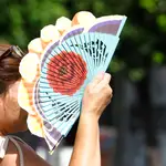 Una mujer se cubre la cara con un abanico mientras camina por el centro de Córdoba