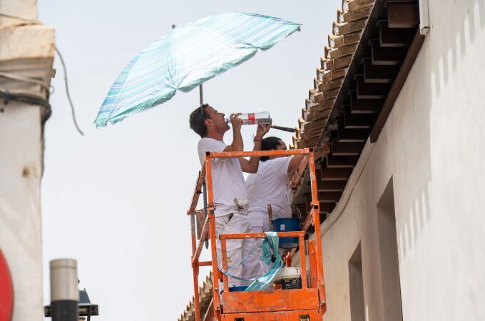  Unos trabajadores se cubren del sol con una sombrilla y beben agua en Andalucía