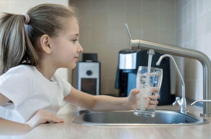 Una niña se sirve un vaso de agua del grifo