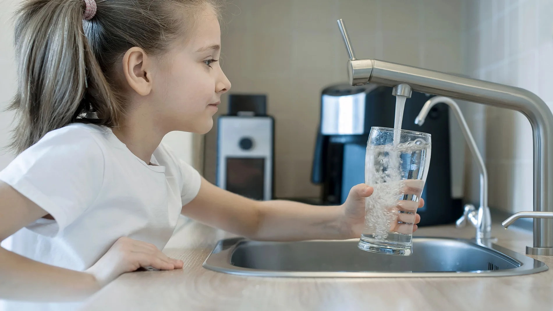Una niña se sirve un vaso de agua del grifo