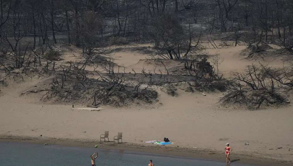 Dos bañistas juegan con una pelota frente a un bosque quemado en una playa cerca de la aldea de Gennadi en Rodas, una turística isla griega en el mar Egeo, al sureste de Grecia, hoy jueves 27 de julio de 2023
