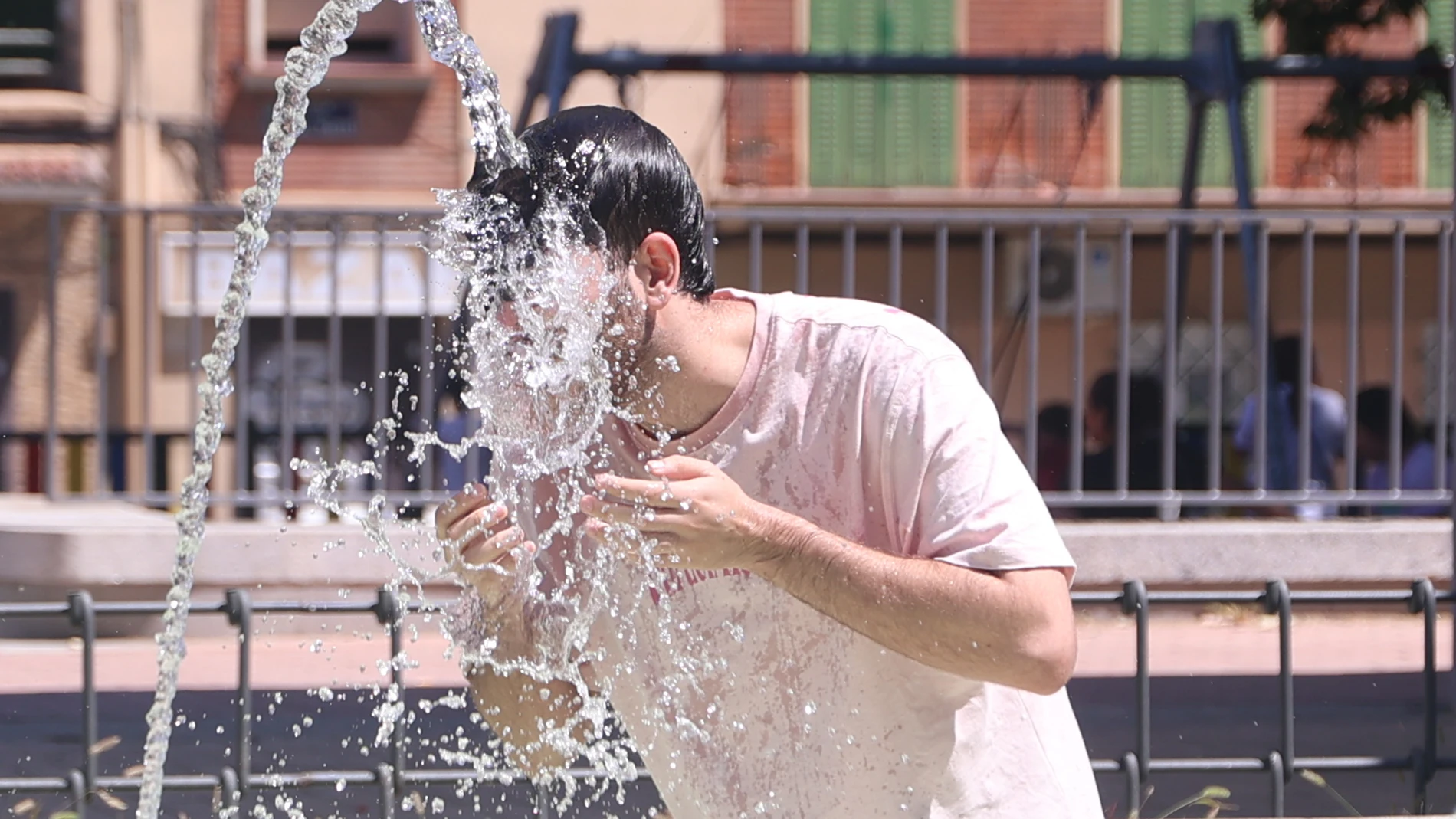 Un joven se refresca en una fuente durante una ola de calor