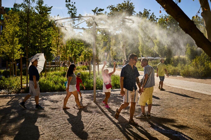 Un grupo de turistas pasa junto a unos aspersores de vapor de agua para intentar refrescarse de la ola de calor que asola Madrid