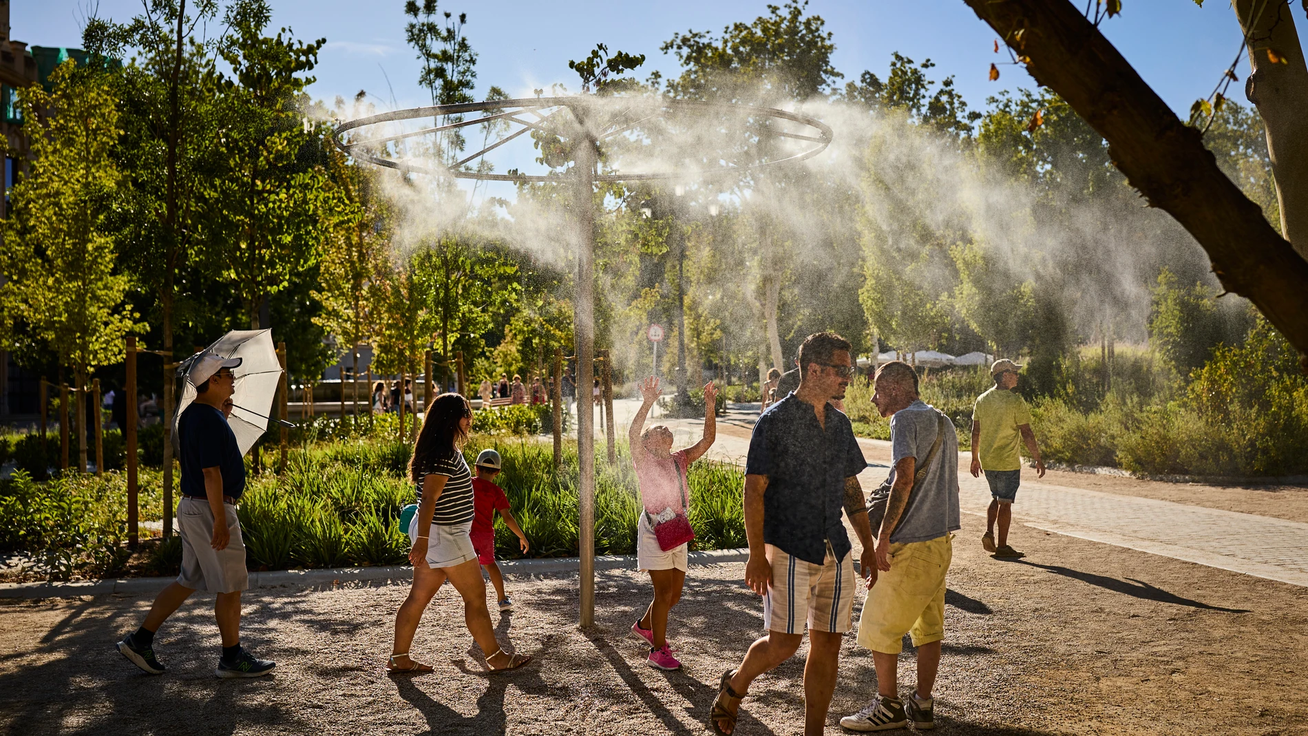 Un grupo de turistas pasa junto a unos aspersores de vapor de agua para intentar refrescarse de la ola de calor que asola Madrid