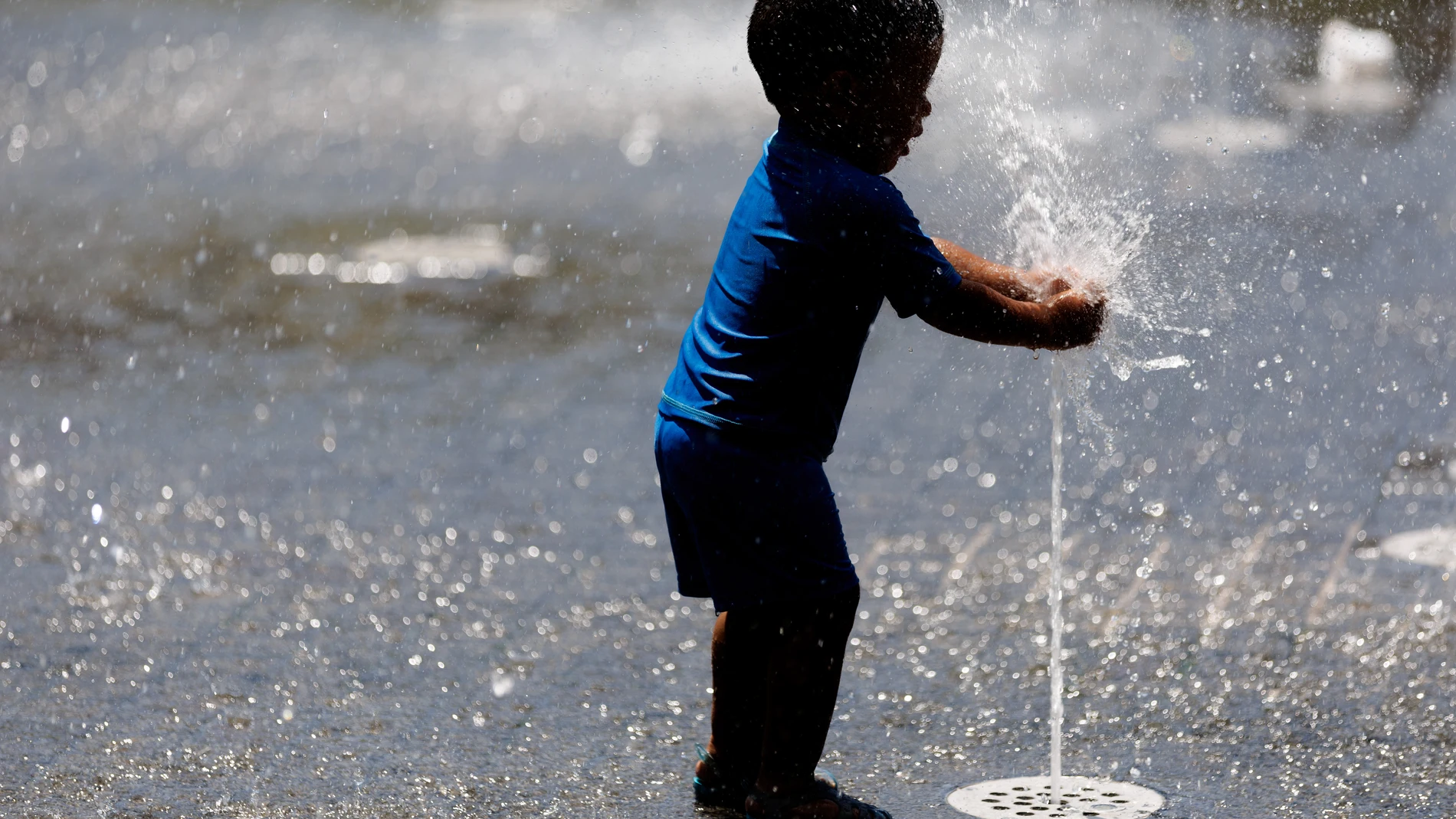 Un niño juega con el agua en una fuente de Madrid